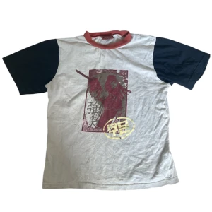 Vit och svart t-shirt med japanskt tryck  - Cool t-shirt i beige med svarta ärmar och röd krage från Disney. Använd men är i bra skick. 