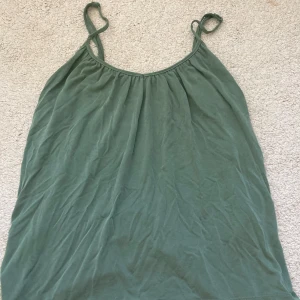 Grön linnetopp från Vero Moda - Säljer en enkel och stilren grön linnetopp från Vero Moda. Toppen har tunna axelband och en lös passform, perfekt för varma dagar. Tillverkad i mjuk bomull som känns skön mot huden.