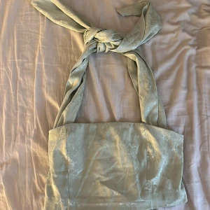  omlottopp  - Supersöt ljusgrön  omlottopp med breda knytband som kan knytas vid axlarna. Toppens tyg har ett subtilt blommigt mönster och en lätt glans. Baksidan är smockad för extra komfort och passform. Perfekt för vår och sommar!