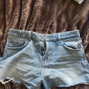 Blå jeansshorts från ZARA - Säljer ett par klassiska blå jeansshorts från ZARA med fransade kanter. Shortsen är regular/ low waisted. Tidlös denim-look som passar till det mesta. Stl 36. Hör av er om ni undrar något❤️