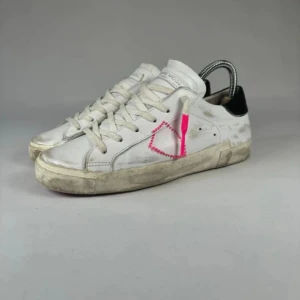 Philippe Model Skor - Snygga vita sneakers från Philippe Model med svart häl och en unik rosa broderad detalj på sidan. Skorna har snörning och röd sula, tillverkade i skinn. Perfekta för dig som vill sticka ut med en cool detalj.  Skick 9/10 