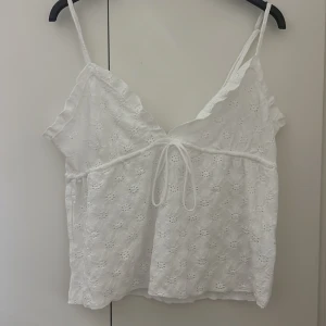 Vit broderad linnetopp från 157 - Säljer en söt vit linnetopp från 157 med broderade blommor och tunna axelband. Toppen har volangdetaljer vid bysten och knytning framtill. Perfekt för varma dagar och somriga outfits! Skriv om ni vill sänka priset, kan sänka priset väldigt lågt eftersom att jag inte vill ha kvar den