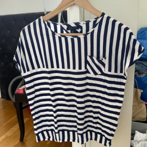 Randig t-shirt från Tommy Hilfiger - Säljer en blåvit randig t-shirt från Tommy Hilfiger. T-shirten har korta ärmar, rund halsringning och en liten bröstficka. Tillverkad i mjuk bomull och har både vertikala och horisontella ränder för en cool look. (Barn storlek xl, vuxen ca xs)