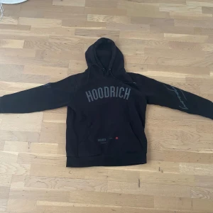 Svart hoodie från Hoodrich - Svart hoodie från Hoodrich med stor logga på bröstet och tryck på ena ärmen. Klassisk huva och känguruficka framtill. Perfekt för en avslappnad streetwear-look. Pris kan diskuteras😃