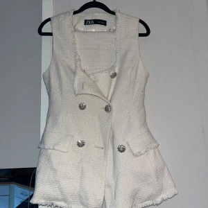 Vit tweed set med glittriga knappar Zara  - Snygg vit väst och utsvängda byxor från Zara i tweedliknande material med glittriga silverknappar framtill. Västen har fransade kanter, fickor och en lätt figursydd passform. Perfekt för att lyfta en outfit med en chic touch.