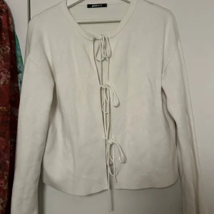 Vit kofta med snörning från Gina Tricot - Superfin vit kofta från Gina Tricot med snörning framtill. Koftan är stickad, har lång ärm och en clean, enkel look som passar till allt. Perfekt att slänga över en topp för en chill vibe. Snygg och trendig modell med normal passform.