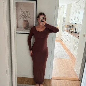 Brun långärmad långklänning - Snygg brun långklänning med lång ärm och rundad urringning. Klänningen har en tight passform som framhäver figuren och är enkel i stilen utan mönster eller extra detaljer. Perfekt för dig som gillar stilrena och minimalistiska plagg.
