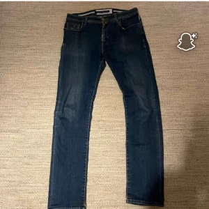 Blå jeans från Jacob Cohën - Blå jeans från Jacob Cohën med klassisk femficksdesign och läderpatch med logga bak. Jeansen har raka ben och diskreta slitningar för en cool, avslappna look. 