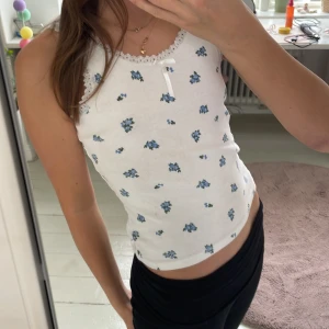 Vit blommig linnetopp med spets - Supersöt vit linnetopp med små blå blommor och spetskant vid halsringningen. Toppen har smala axelband och en liten rosett framtill. Perfekt för en somrig look och passar till både jeans och kjol. Pris kan diskuteras!🥰