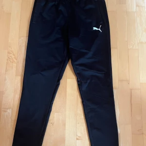 Svarta träningsbyxor från Puma L - Svarta träningsbyxor från Puma i storlek L. Byxorna har elastisk midja, raka ben, fickor och Puma-logga på ena låret. Perfekta för träning eller chill.