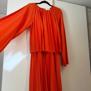  range långklänning med volanger från ASOS - Säljer en maxilång, plisserad klänning från ASOS DESIGN i en riktigt snygg orange färg. Klänningen har långa ärmar och ett flowigt fall med breda veck. Perfekt för dig som vill sticka ut med en färgstark look. Endast använd 2-3 gånger och klänningen är i nyskick.