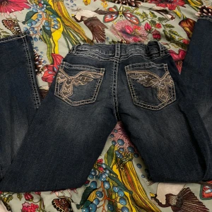 Mörkblå jeans med broderade fickor Gina Tricot - Snygga mörkblå jeans från Gina Tricot i storlek 158. Jeansen har vita kontrastsömmar och coola broderade bakfickor med glittriga detaljer. Klassisk femficksmodell med knapp i silverfärg och bälteshällor. Perfekt för dig som gillar detaljer och vill sticka ut.
