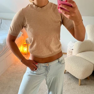 Beige stickad kortärmad topp - Säljer en beige stickad topp med korta ärmar och rund hals. Modellen är croppad och har ribbade kanter vid hals, ärmslut och nederkant. Perfekt för dig som gillar en enkel och stilren look med en mjuk känsla.