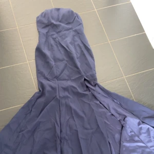 Marinblå balklänning med släp  - Säljer en marinblå långklänning med axelbandslös och figurnära överdel. Klänningen har ett elegant, svepande fall och är tillverkad i ett mjukt, glansigt tyg som ger en lyxig känsla. Perfekt för dig som vill sticka ut med en stilren och klassisk look.