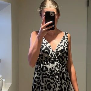 Leopardmönstrad långklänning Saint Tropez - Snygg långklänning från Saint Tropez i leopardmönster med svart och beige toner. Klänningen har omlott-v-ringning och är ärmlös, med ett lätt och flowigt fall. Tillverkad i 100% polyester, perfekt för dig som gillar att sticka ut med djurmönster.