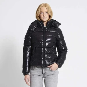 Svart glansig pufferjacka  - Säljer en svart, glansig pufferjacka med huva och dragkedja framtill. Jackan har quiltad design, lång ärm. Perfekt för kalla dagar när du vill vara både varm och snygg. Väldigt svår att få tag på. xs/s