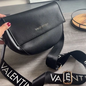 Valentino väska - Snygg svart axelväska från Valentino med stilren design och rundad form. Har använts en del men används inte längre. Köpt för 1200💕