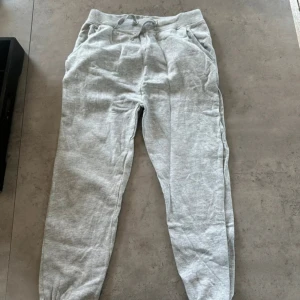 Grå mjukisbyxor med snörning - Ljusgrå mjukisbyxor från 157 med resår och snörning i midjan. Byxorna har ribbade muddar vid bensluten och två sidofickor. Perfekta för chill eller träning, tillverkade i mjukt bomullsmaterial.