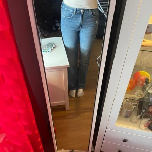 Blå bootcut jeans med hög midja - Säljer ett par snygga blå jeans med bootcut-modell och hög midja. Jeansen har klassiska fem fickor, dragkedja och knapp framtill. 
