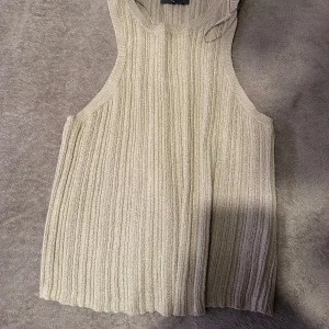 Beige ribbad ärmlös linnetopp - Snygg beige linnetopp med ribbad struktur och ärmlös design. Perfekt för varma dagar och enkel att matcha med jeans eller kjol. Tidlös och stilren modell som passar till många olika looks.