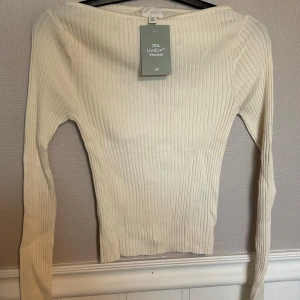 Ribbad vit långärmad topp H&M - Ribbad långärmad topp från H&M i en fräsch vit färg. Toppen är figurnära och har en stilren, enkel design med rund halsringning. Tillverkad i 70% LivaEco viskos för en mjuk och skön känsla. Perfekt att styla med jeans eller kjol.