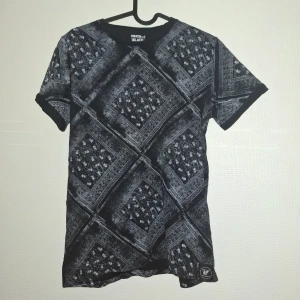 Svart mönstrad t-shirt RG512 Black Label - Cool svart t-shirt från RG512 Black Label med unikt rutmönster i grått och vitt. T-shirten har rund hals och korta ärmar, perfekt för dig som gillar streetstyle. Materialet är mjukt och skönt, troligtvis bomull. Snygg detalj med logga nertill på framsidan.