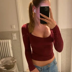 Vinröd långärmad topp från Nelly - Säljer en vinröd långärmad topp från Nelly i storlek XXS. Toppen har en tight passform, croppad längd och en snygg v-ringad urringning med spetskant. Perfekt att styla med jeans eller kjol för en trendig look. se bild 2 för två små hål på armen 