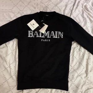 Balmain Paris sweatshirt - Svart sweatshirt från Balmain Paris med stor vit logotyp framtill. Klassisk rund halsringning och långa ärmar. Tillverkad i mjuk bomull för en skön och stilren look. Perfekt för dig som gillar exklusiva streetwear-vibbar.
