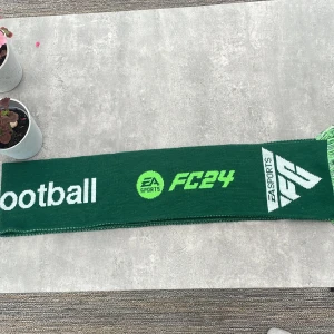 Grön EA Sports FC24 halsduk - Snygg grön halsduk med texten 'total football', EA Sports FC24-logga och Lack of Guidance-mönster. Halsduken har vita och ljusgröna detaljer samt fransar i ändarna. Perfekt för dig som älskar fotboll och gaming.