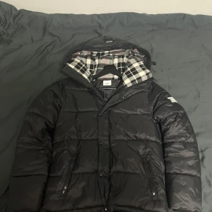 Svart pufferjacka från Burberry - Det är jacka versionen, inte väst. om du behöver fler bilder eller har fråga så är det bara skriva. Säljer en svart pufferjacka från Burberry med klassiskt rutigt foder i svart, vitt och lite rött. Jackan har huva, dragkedja och knappar framtill samt två fickor med dragkedja. 