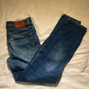 Jack & Jones blå jeans Regular Clark - Snygga blå jeans från Jack & Jones i modellen Regular Clark. Klassisk femficksdesign med bruna sömmar och läderpatch bak. Jeansen har en rak passform och är tillverkade i slitstarkt bomullstyg med lätt tvättad look.