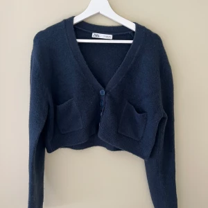 Mörkblå croppad kofta från Zara - Mysig mörkblå croppad kofta från Zara med två stora fickor framtill och v-ringad hals. Koftan har långa ärmar och stängs med knappar. 