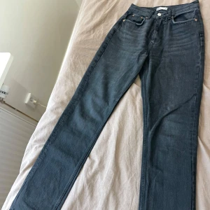 Svarta raka jeans från Gina Tricot - Säljer ett par svarta jeans från Gina Tricot med hög midja och raka ben. Jeansen har klassisk femficksdesign, knapp och dragkedja framtill samt diskreta nitar vid fickorna. Perfekta till en avslappnad och stilren look.