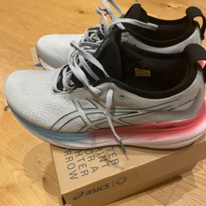 ASICS Gel-Nimbus PureGEL sneakers- nya,  använda en gång   - Lätta och snygga ASICS Gel-Nimbus sneakers i ljusgrått med svarta och rosa detaljer. Ovandel i ventilerande syntetmaterial, svart innersula och cool gradient på sulan från rosa till blått. Perfekta för dig som ofta får ont löpning eller träning, då de har extra bekväm dämpning!                       Köpta  för 2500 nu 1200. Använda en kort löprunda, var för små för sonen. Finns i Älvsjö eller skickas. 