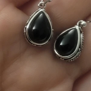 Helt nya Droppformade örhängen i silver och svart - Snygga örhängen med droppformad svart sten infattad i detaljerad silverram. Hängande modell med fina snirkliga mönster runt kanterna som ger en unik och elegant vibe. Perfekta för dig som gillar klassiska smycken med en twist.