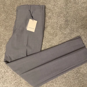 Grå kostymbyxor från Corneliani - Snygga grå kostymbyxor från lyxmärket Corneliani helt oanvända med lapppriset fortfarande på köpt som present och passar tyvärr inte mig därför säljs ny pris är cirka 3000 kr på hemsidan någon som söker efter klass och ett lyxigt material är detta perfekt för storlek 52 regular fit 