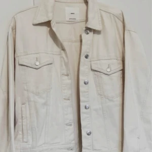 Beige jeansjacka från Mango - Säljer en stilren beige jeansjacka från Mango. Jackan har en klassisk krage, knappar framtill och två bröstfickor med lock. Perfekt för en avslappnad look.