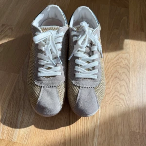 Beige sneakers från Blauer - Snygga beige sneakers från Blauer med vit snörning och en stilren design. Skorna har en mesh-liknande textur på sidorna och mockadetaljer vid tån och hälen. Perfekta för en avslappnad stil.