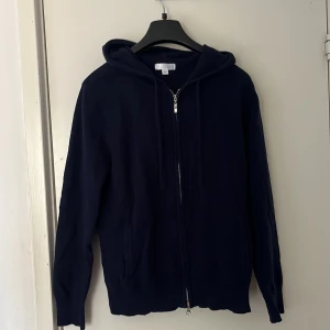 Mörkblå ull kofta från Barlucio - Säljer en stilren mörkblå kofta från Barlucio. Tröjan har en praktisk dragkedja framtill och en bekväm huva. Perfekt för en avslappnad look. Koftan passar storleken S-M.