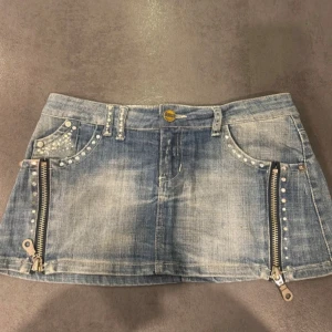 Jeanskjol med dragkedjor och nitar - Snygg jeanskjol i blått med dragkedjor framtill samt glitter. Fickorna har även väldigt fina detaljer. Säljer då den är för liten. I bra skick. 