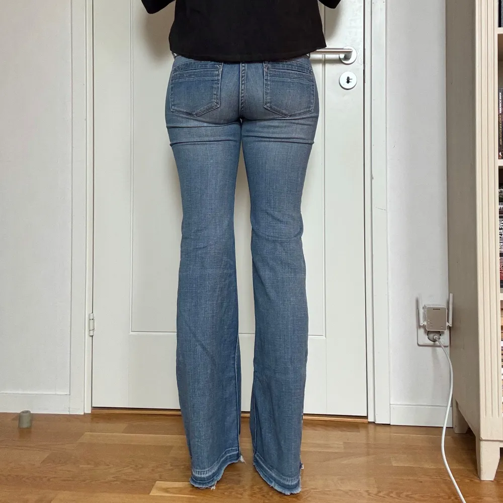Snygga blå bootcut jeans med slitningar på låren och hål på knäna. Jeansen har en lågmidjad passform och är tillverkade i ett bekvämt denimtyg. Storlek 28x32. Jag är ca 177 cm. Midjemåttet är ca 80 cm, innerbenslängden är ca 88 cm och grenmåttet är ca 21 cm. En liten defekt på baksidan som tidigare varit ett hål som är igen sytt, syns på sista bilderna.. Farkut & Housut.