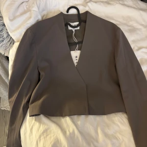 Grå kavaj från NA-KD - Snygg grå kavaj från NA-KD med en modern croppad design. Kavajen har en stilren v-ringad öppning och långa ärmar. Perfekt för en vår look. Köpt för 599
