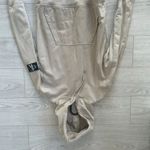Beige hoodie från Calvin Klein Jeans - Säljer en stilren beige hoodie från Calvin Klein Jeans. På ärmen finns en svart patch med CK-loggan. Knappt använd och precis som ny