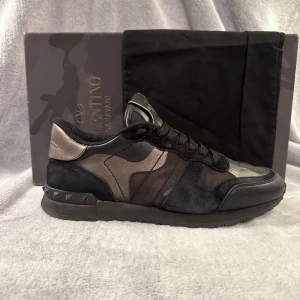 Valentino rockrunners  - Snygga Valentino Garavani sneakers med ett coolt camouflagemönster i svart och grått. Skorna har snörning och en robust sula med nitar på hälen för extra stil. Perfekta för att ge din outfit en edgy touch. Hör av er vid minsta frågor 😄 mvh CH