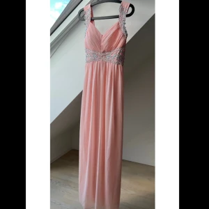 Balklänning från Cotton Club - Fin balklänning från Cotton Club med v-ringad design och vackra paljettdekorationer. Klänningen har breda axelband och en smickrande passform med rynkade detaljer. Perfekt för speciella tillfällen.