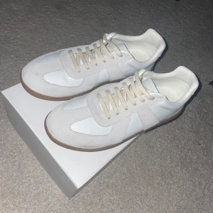 Vita sneakers från Maison Margiela - Snygga vita sneakers från Maison Margiela i storlek 44. Använda 2-3 gånger så Inga defekter eller permanenta fläckar. Ny pris är 7000kr, hör av er vid frågor.