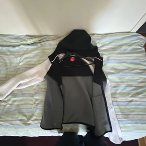 Svart och vit jacka från Nike - Säljer en stilren svart och vit jacka från Nike. Jackan har en huva och är perfekt för en sportig look. Den är tillverkad i syntetmaterial och har en normal passform. Perfekt för vår och höst!