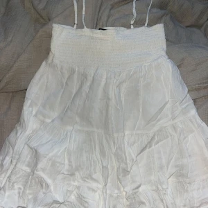 Vit klänning från Zara - Säljer en söt vit klänning från Zara med smala axelband och smockad överdel. Klänningen har en luftig och fladdrig kjol som ger en romantisk känsla. Perfekt för varma sommardagar!