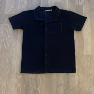 Mörkblå kortärmad skjorta med knappar - Snygg mörkblå kortärmad skjorta med knappar och en bröstficka. Perfekt för en stilren look. Skjortan har en klassisk krage och är tillverkad i ett mjukt material.