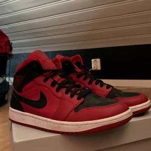 Nike Air Jordans i rött och svart - Säljer ett par klassiska Nike Air Jordans i rött och svart. Skorna har en hög siluett med snörning och den ikoniska Nike-loggan på sidan. Perfekta för dig som vill ha en stilren och sportig look. Skorna är dessutom i nyskick då de endast är använda som högst 3 gånger. Skobox medföljer, köp gärna dessa skor för ett bra och komfortabelt pris😁